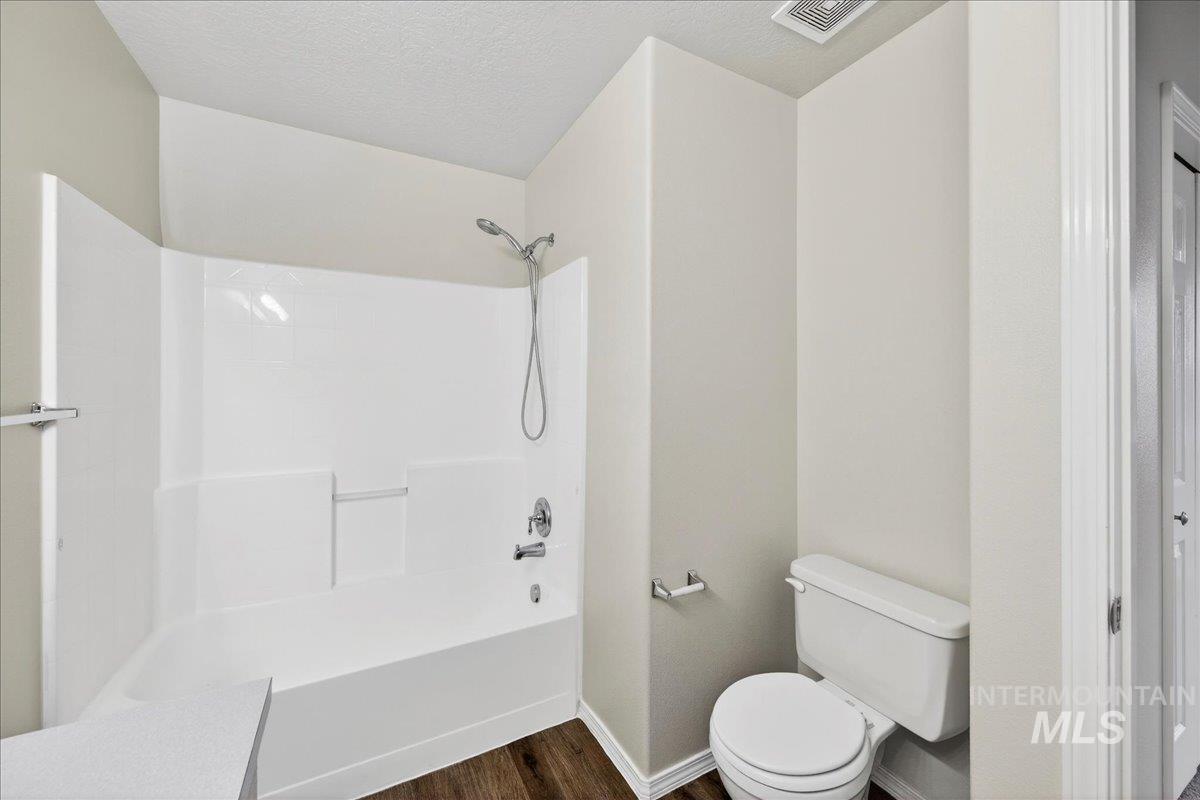 Full bathroom with washtub / shower combination, dark wood finished floors, and a textured ceiling