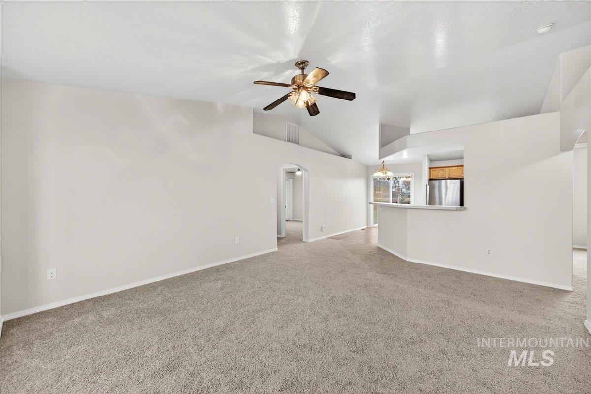 Unfurnished living room featuring arched walkways, carpet flooring, lofted ceiling, a ceiling fan, and a chandelier