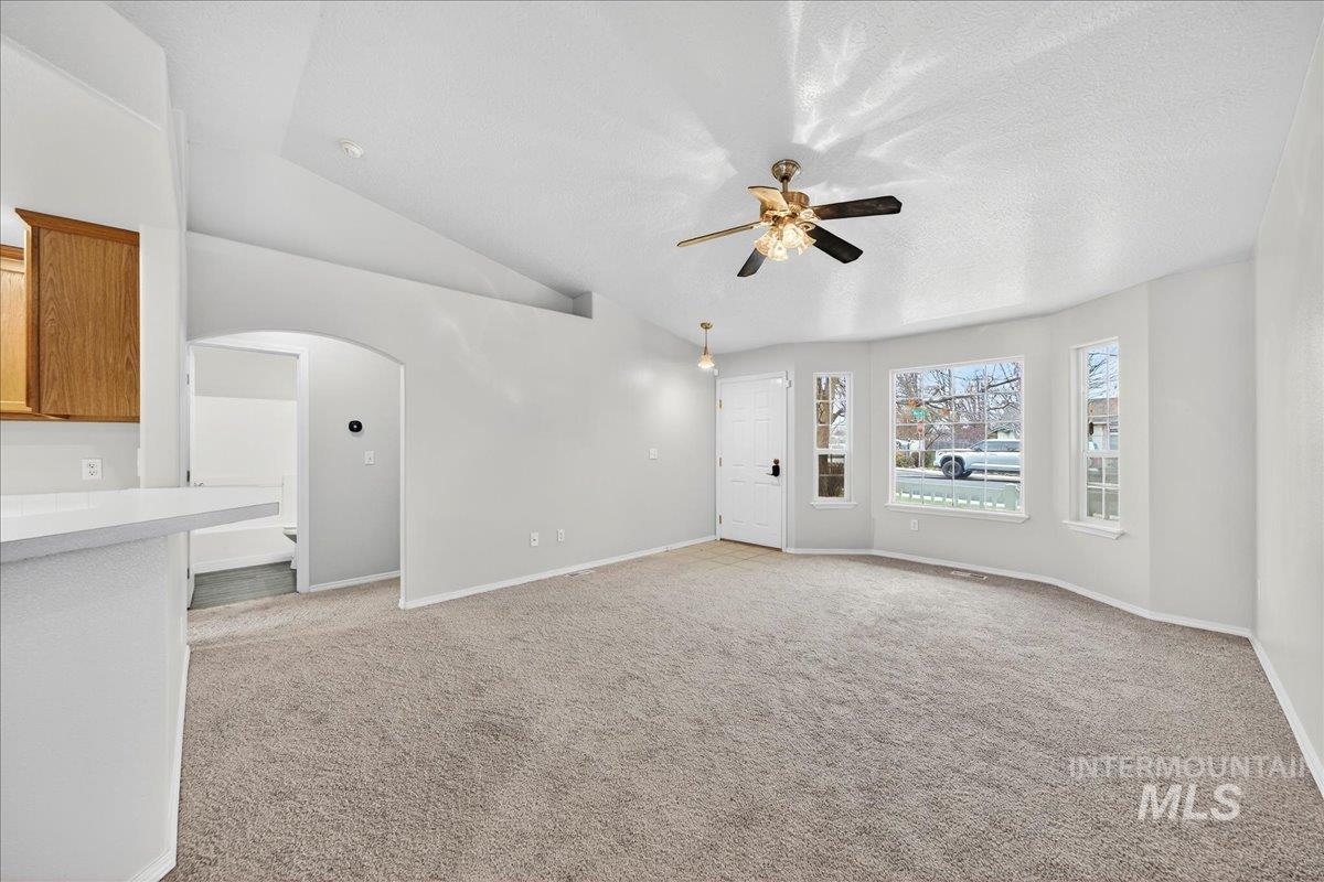 Unfurnished living room with arched walkways, lofted ceiling, light carpet, and a ceiling fan