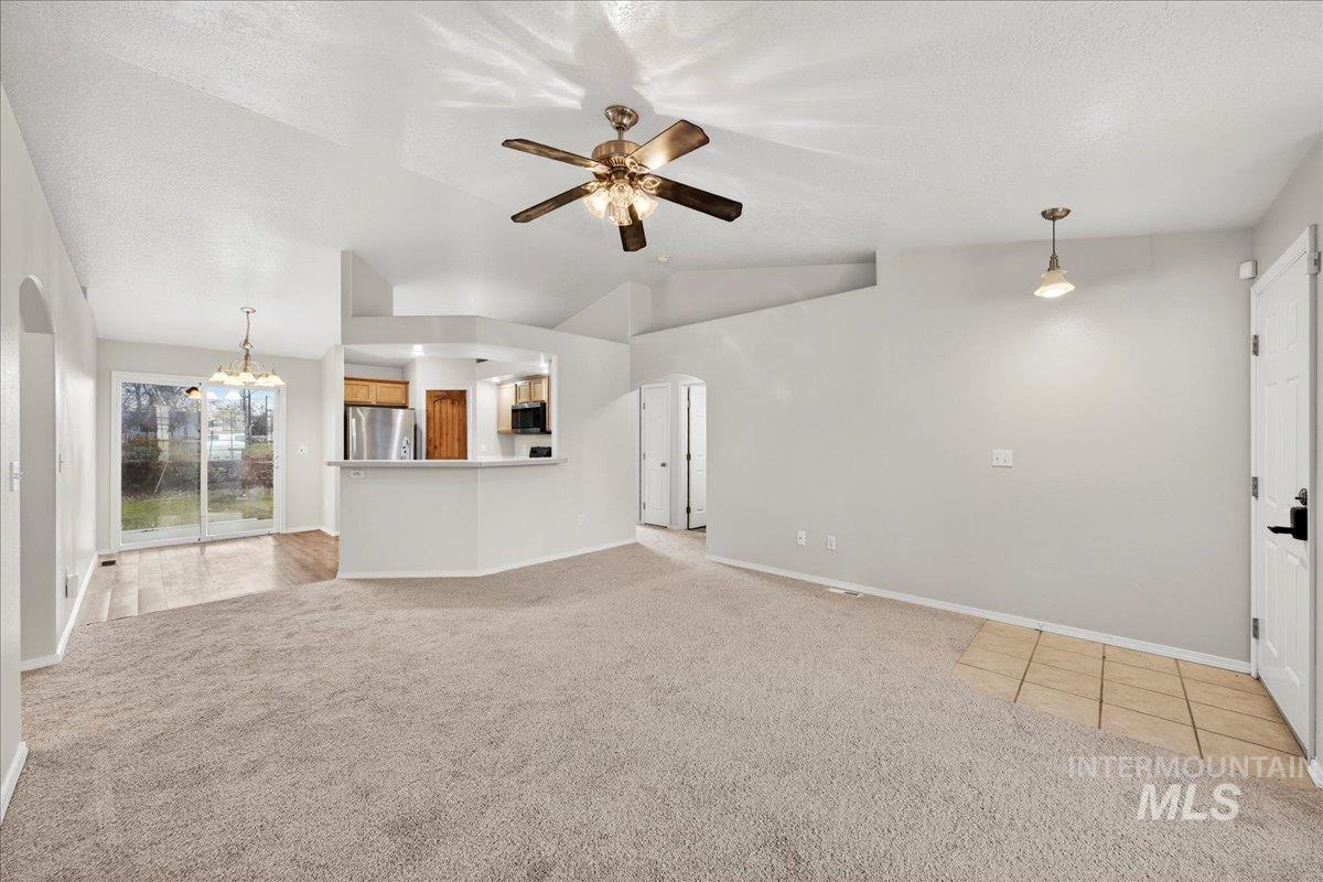 Unfurnished living room featuring arched walkways, light carpet, lofted ceiling, ceiling fan, and a textured ceiling