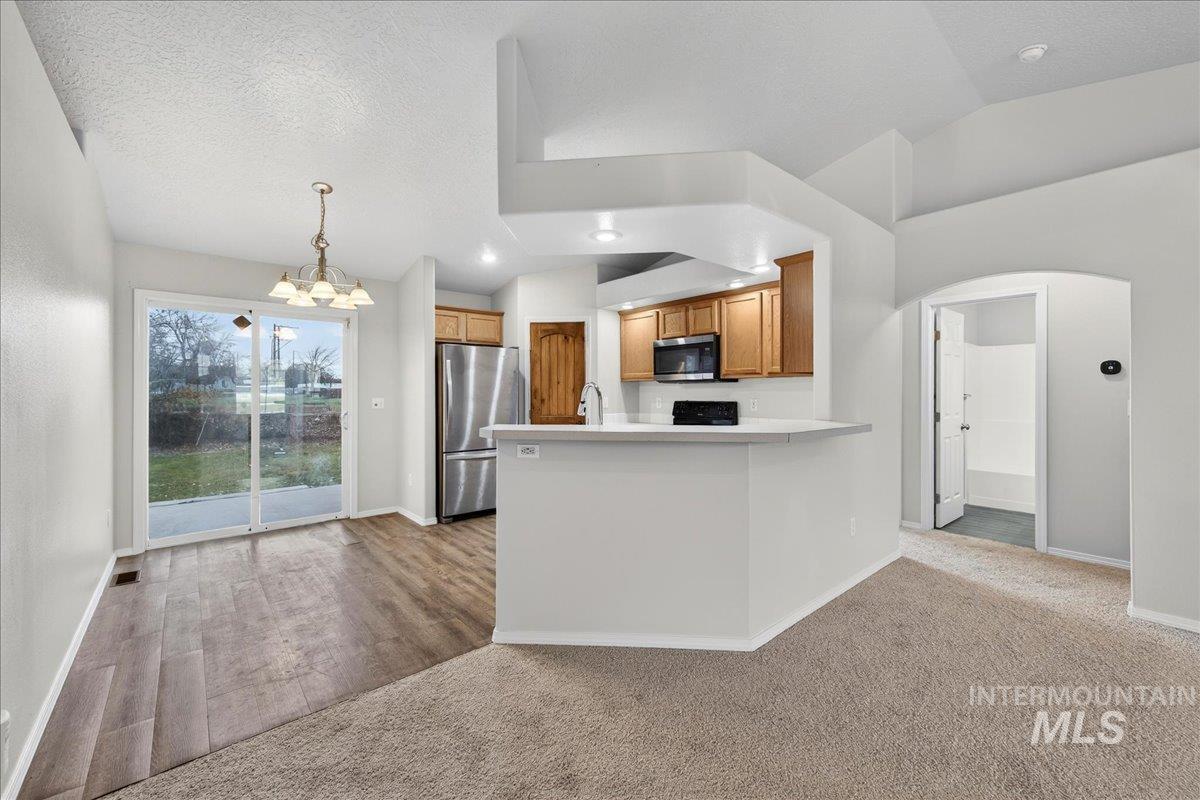 Kitchen featuring arched walkways, brown cabinetry, stainless steel appliances, a chandelier, and a peninsula