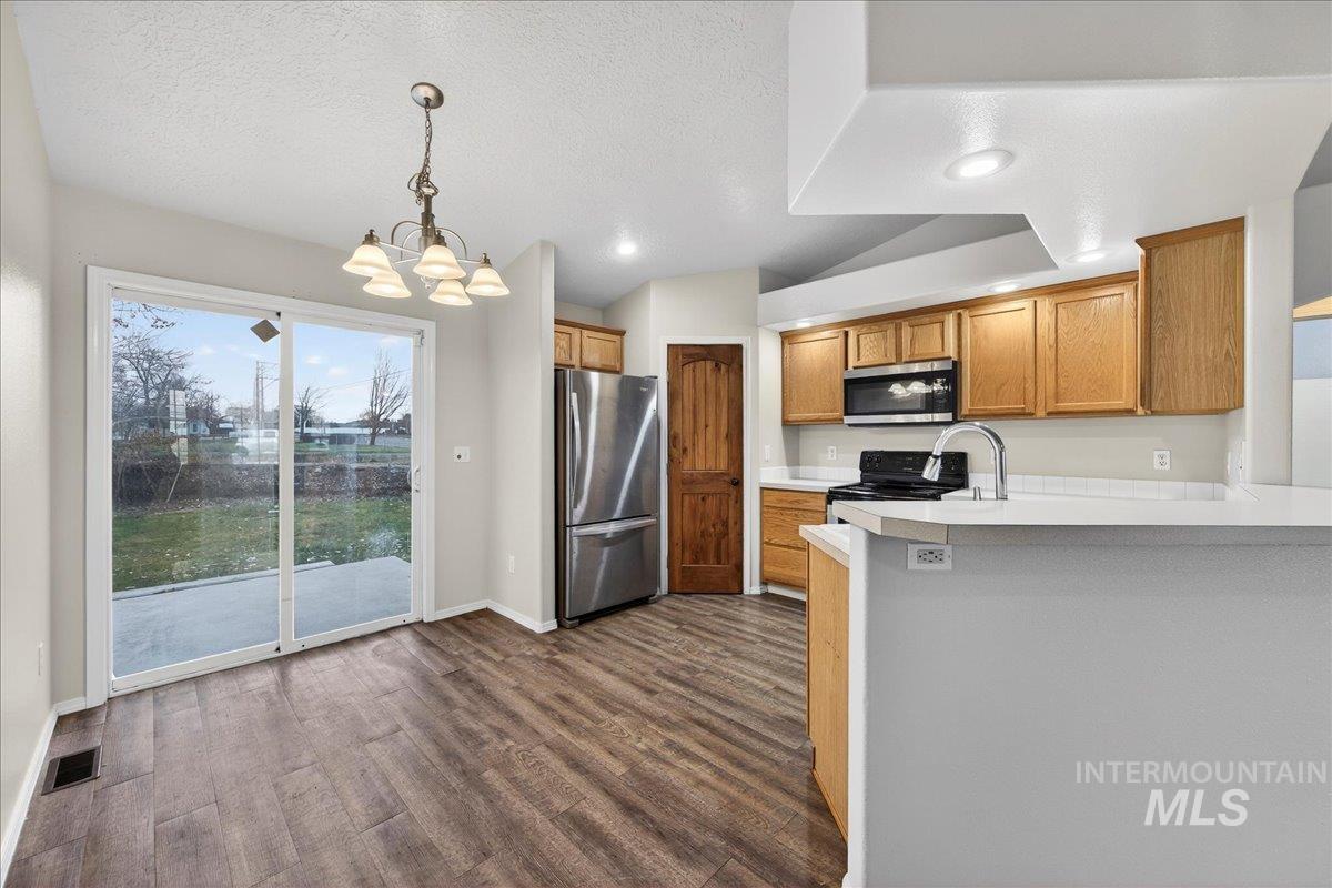 Kitchen featuring appliances with stainless steel finishes, light countertops, decorative light fixtures, dark wood-style flooring, and brown cabinets