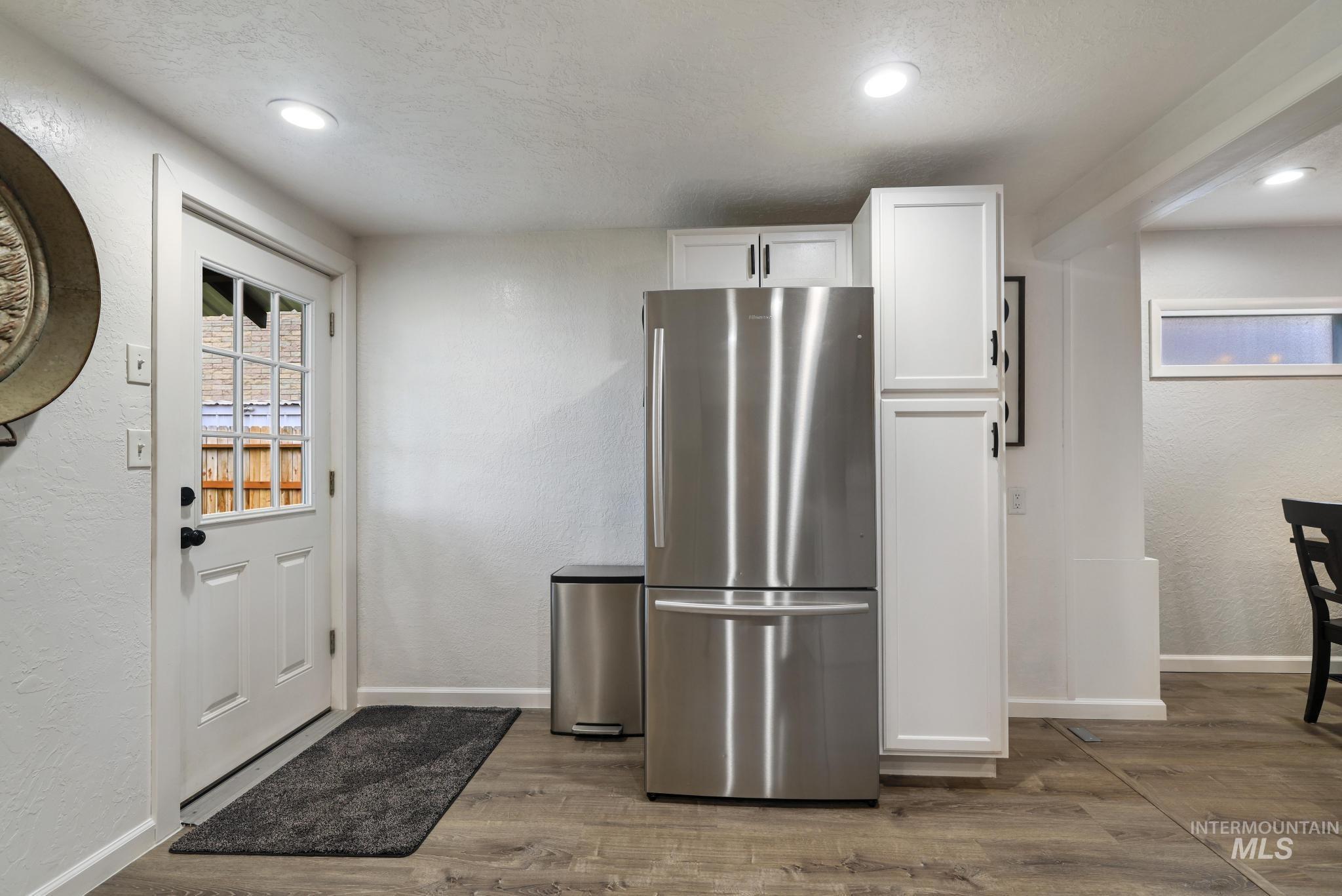 Kitchen featuring a textured wall, white cabinetry, freestanding refrigerator, dark wood-type flooring, and a textured ceiling