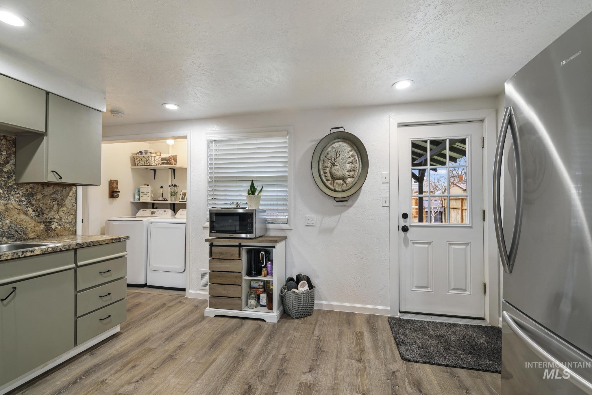 Kitchen with appliances with stainless steel finishes, washing machine and clothes dryer, gray cabinets, light wood finished floors, and green cabinetry