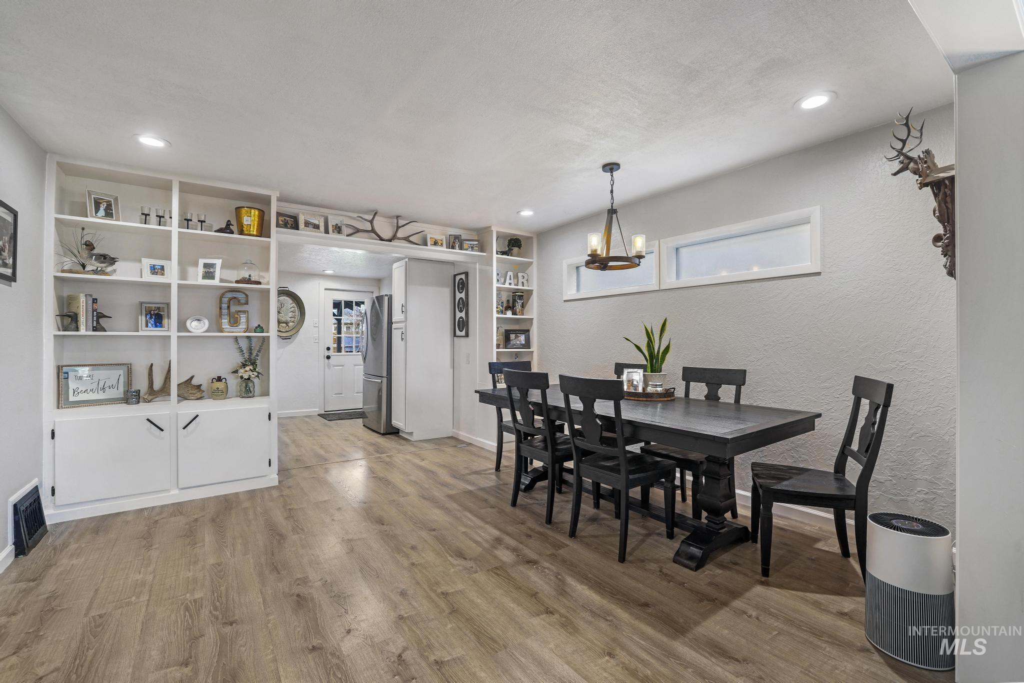 Dining space featuring light wood-type flooring, a textured wall, a chandelier, recessed lighting, and built in shelves