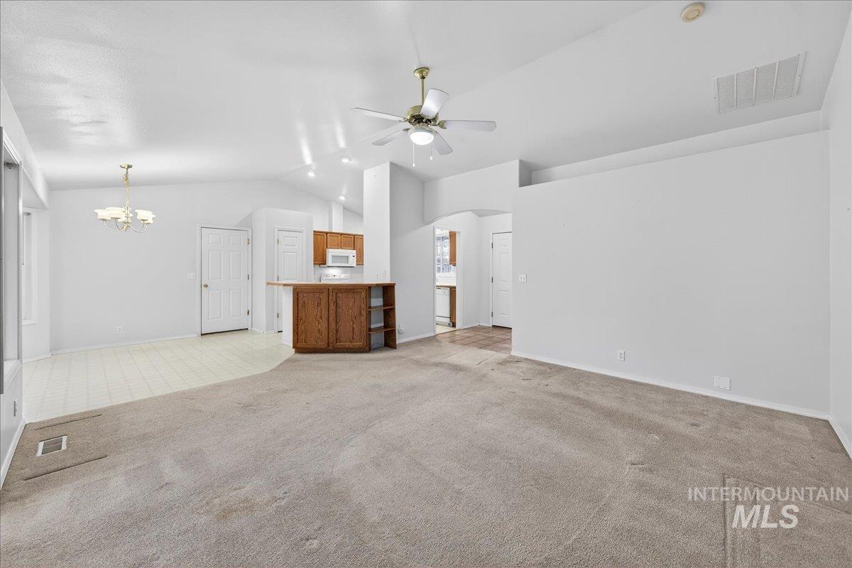 Unfurnished living room featuring lofted ceiling, light colored carpet, a ceiling fan, a chandelier, and arched walkways
