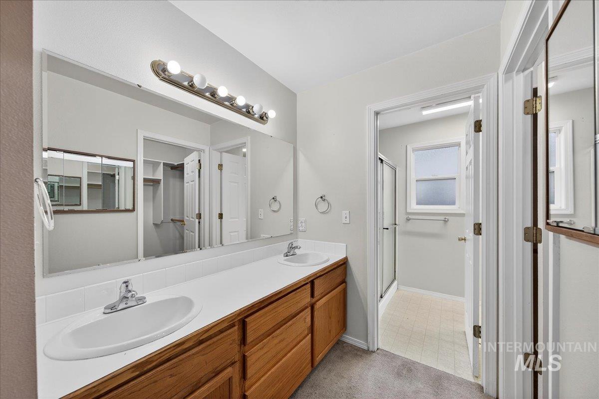 Bathroom with a shower stall, double vanity, light colored carpet, and light flooring