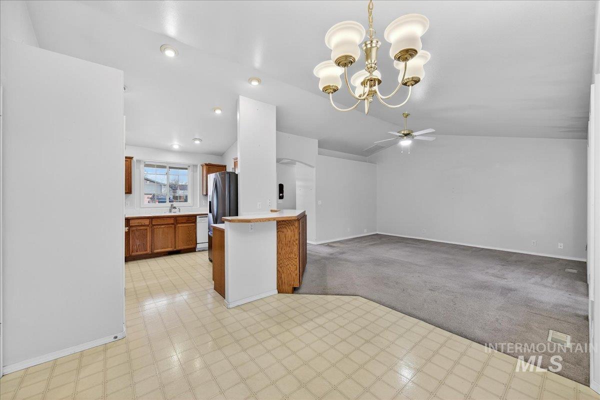 Kitchen with brown cabinets, light colored carpet, decorative light fixtures, light flooring, and vaulted ceiling