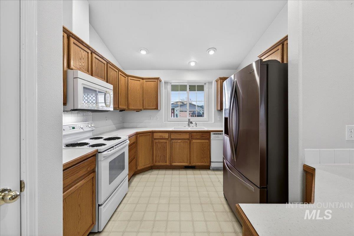 Kitchen featuring light countertops, white appliances, light flooring, brown cabinetry, and recessed lighting