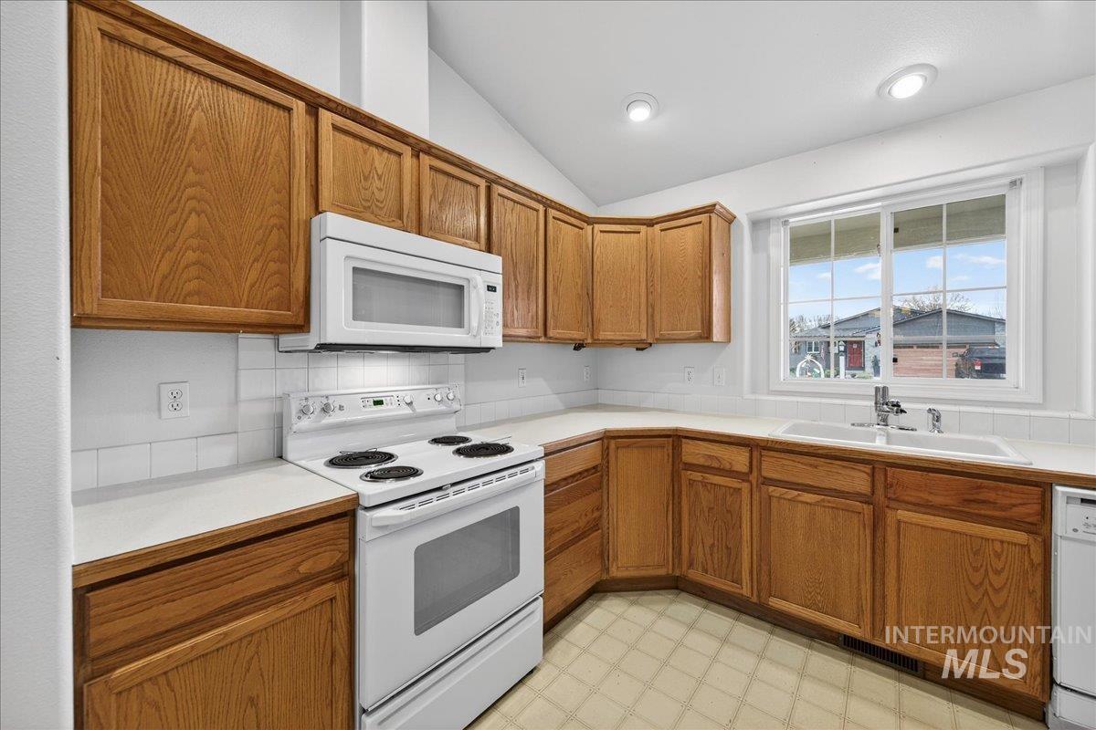 Kitchen with brown cabinets, white appliances, light countertops, light floors, and lofted ceiling