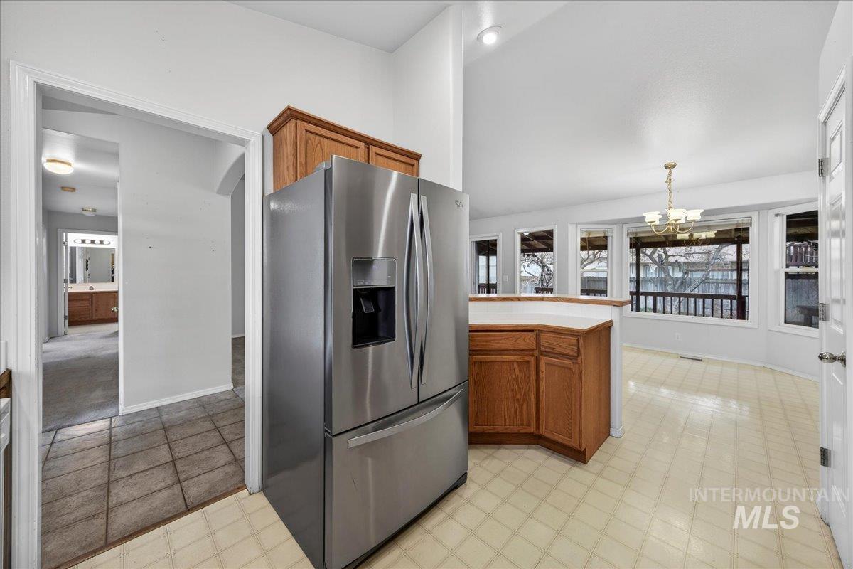 Kitchen with brown cabinets, stainless steel fridge, light floors, pendant lighting, and a chandelier