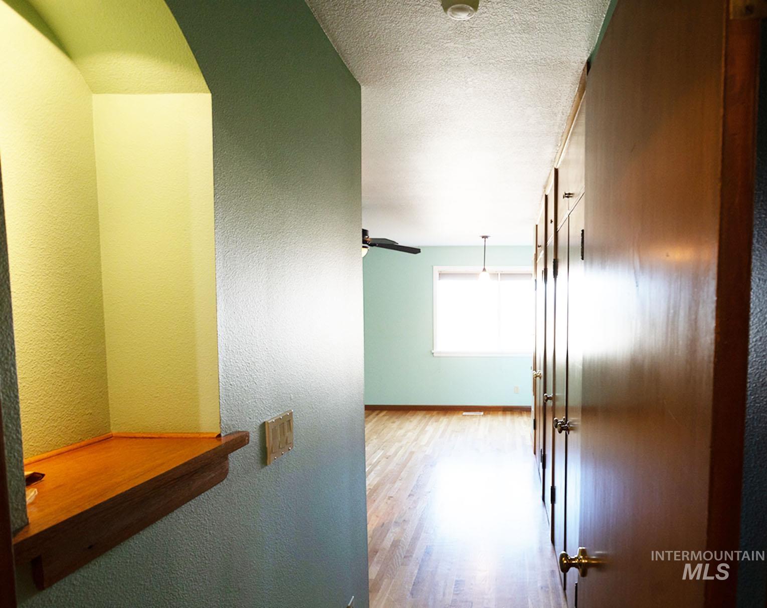 Corridor featuring a textured wall, light wood finished floors, and a textured ceiling