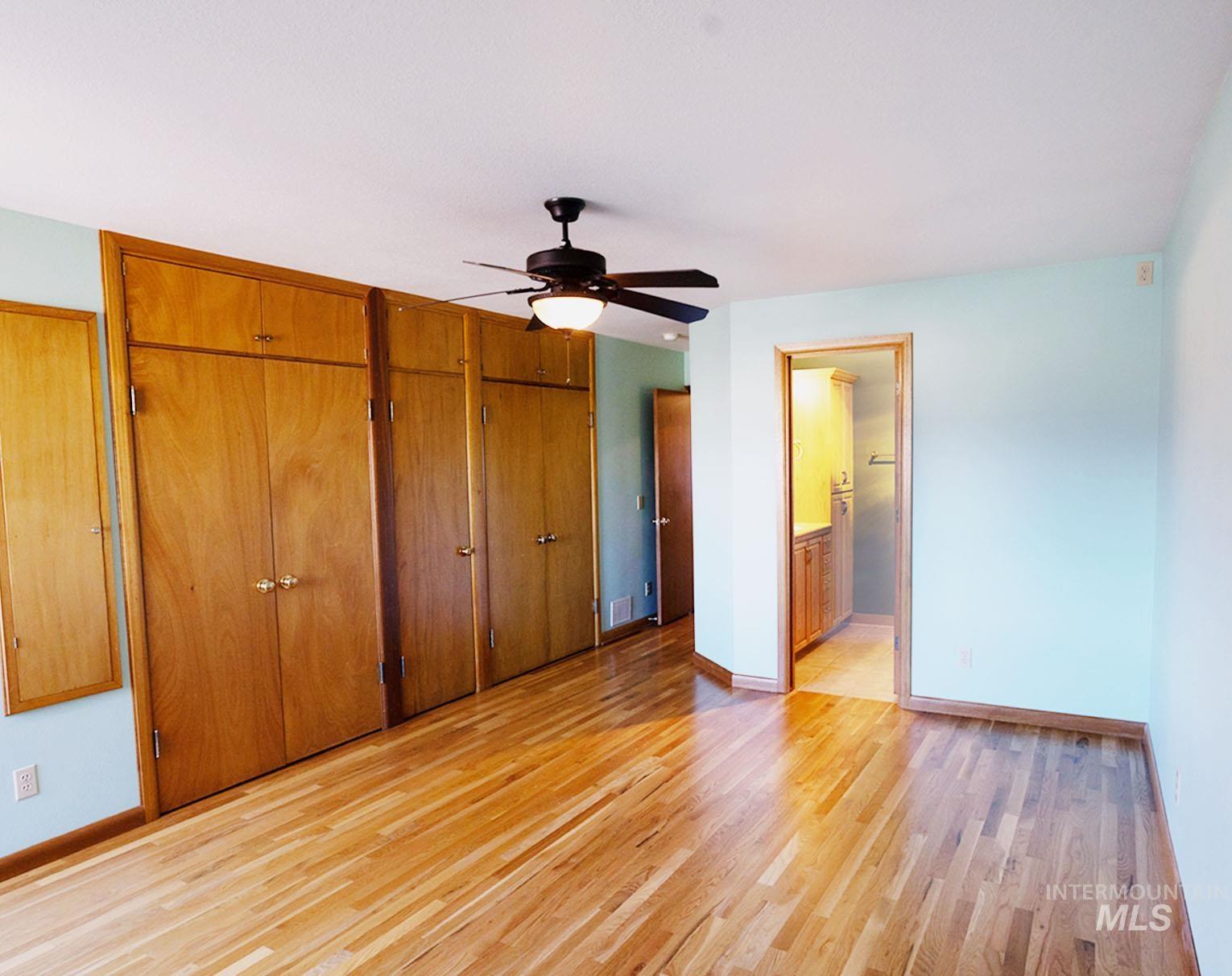 Unfurnished bedroom featuring two closets, light wood-type flooring, a ceiling fan, and ensuite bathroom