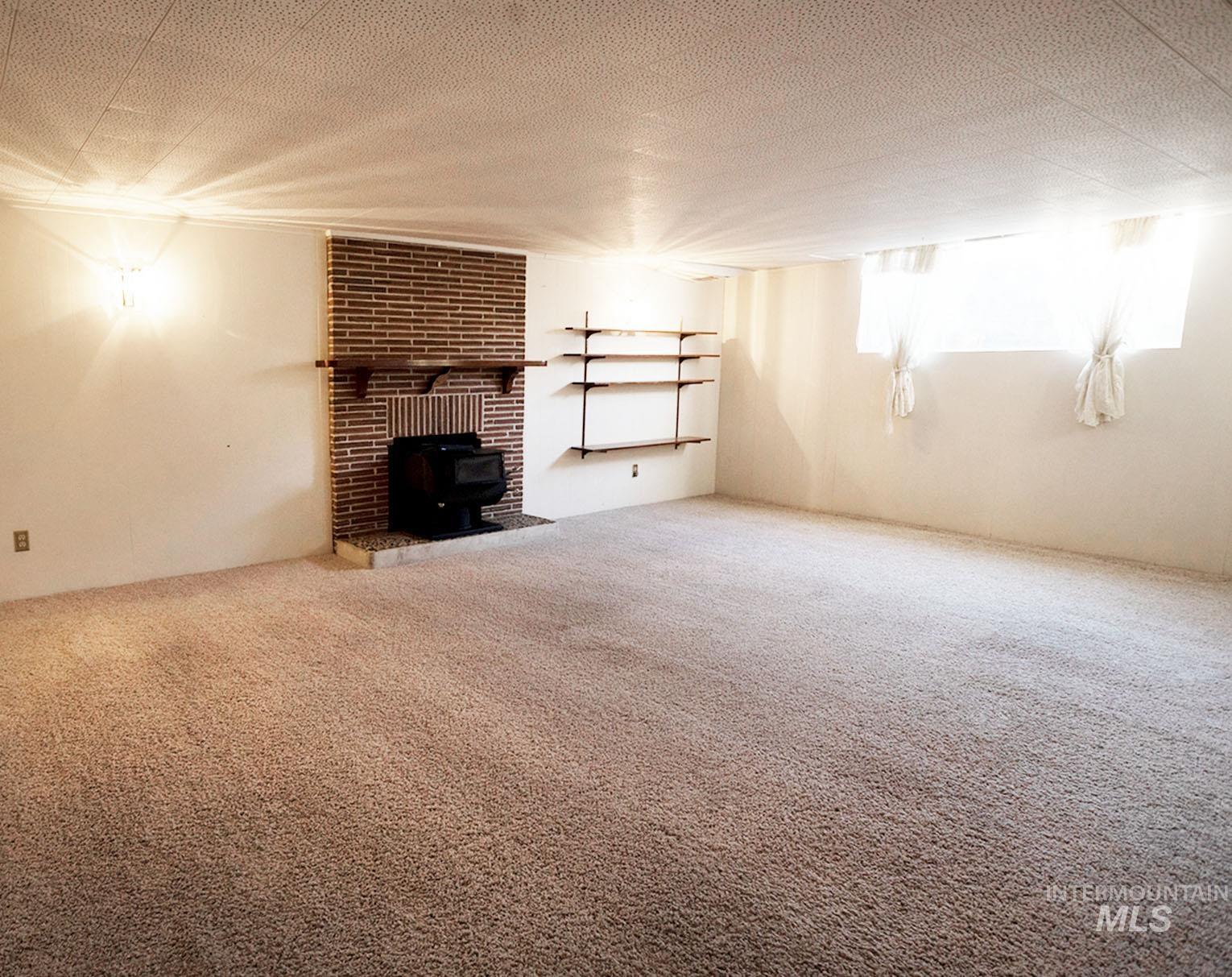 Unfurnished living room featuring carpet flooring, a wood stove, and a textured ceiling