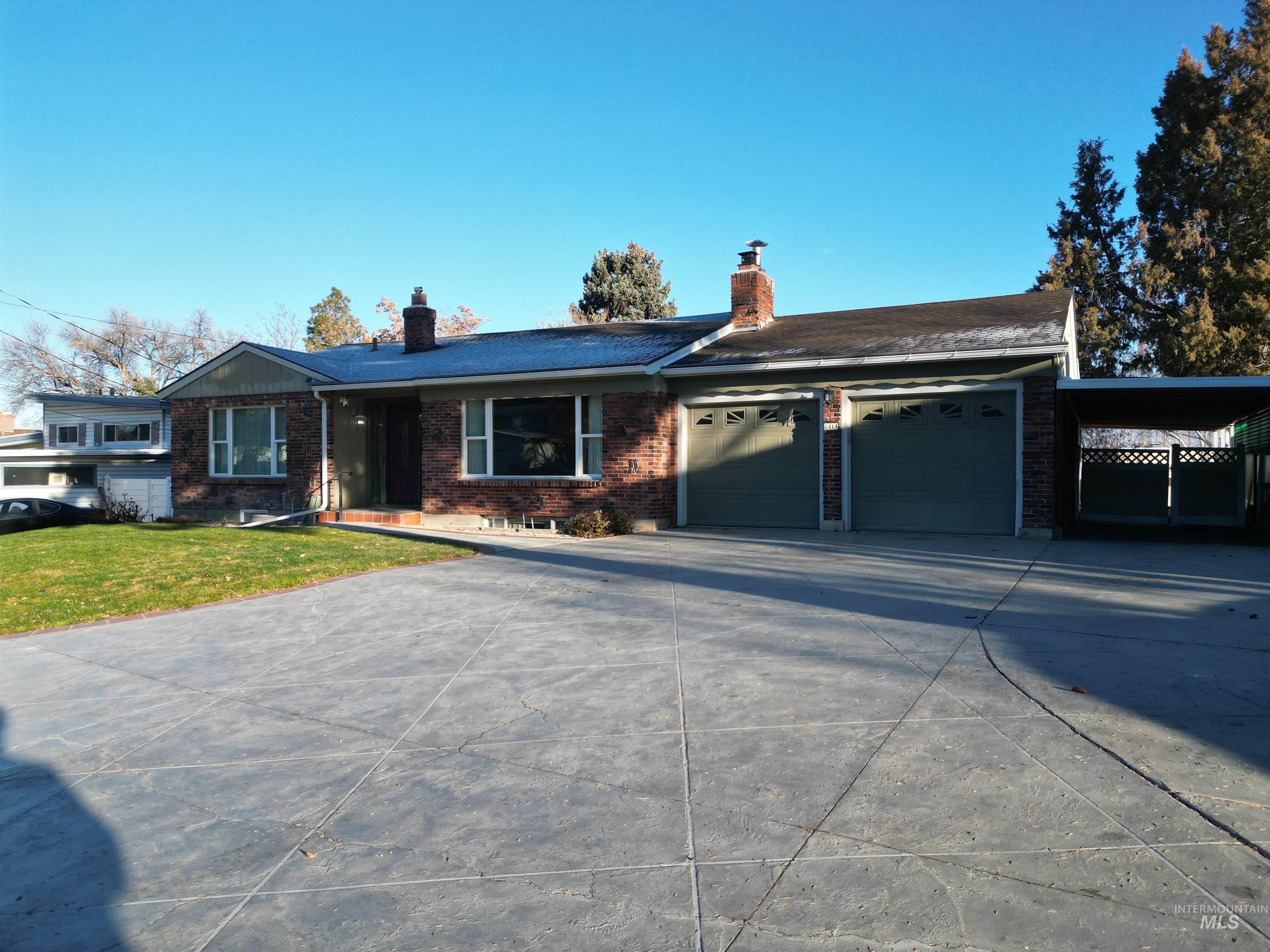 Ranch-style house featuring a chimney, concrete driveway, a front yard, brick siding, and a garage