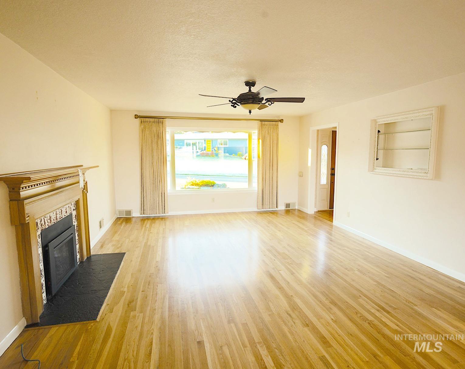Unfurnished living room with light wood-style flooring, a tile fireplace, a textured ceiling, and a ceiling fan