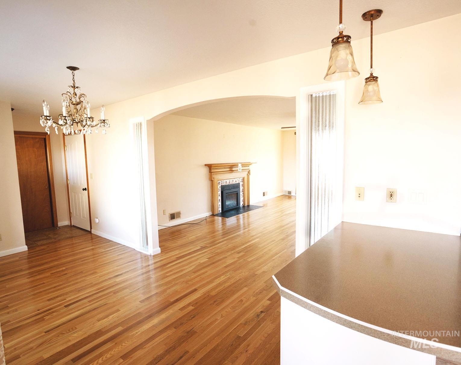 Unfurnished living room featuring light wood-style floors, a tiled fireplace, a chandelier, and arched walkways