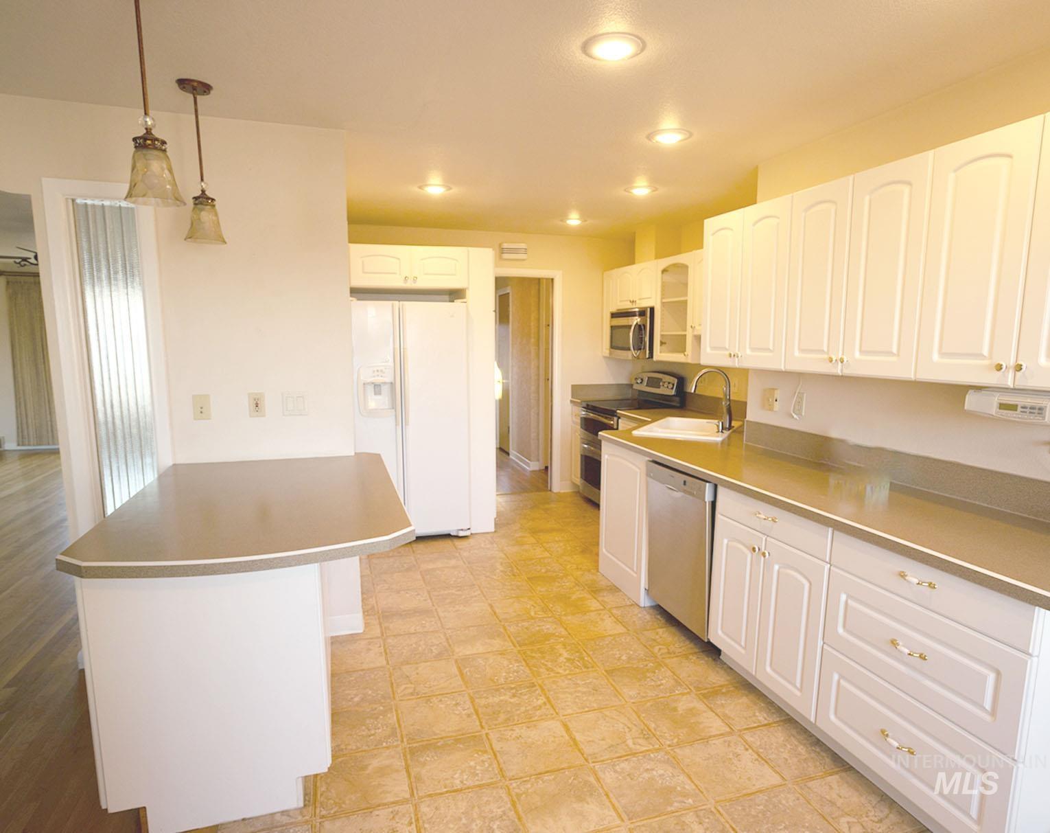 Kitchen featuring appliances with stainless steel finishes, decorative light fixtures, white cabinetry, stainless steel counters, and recessed lighting