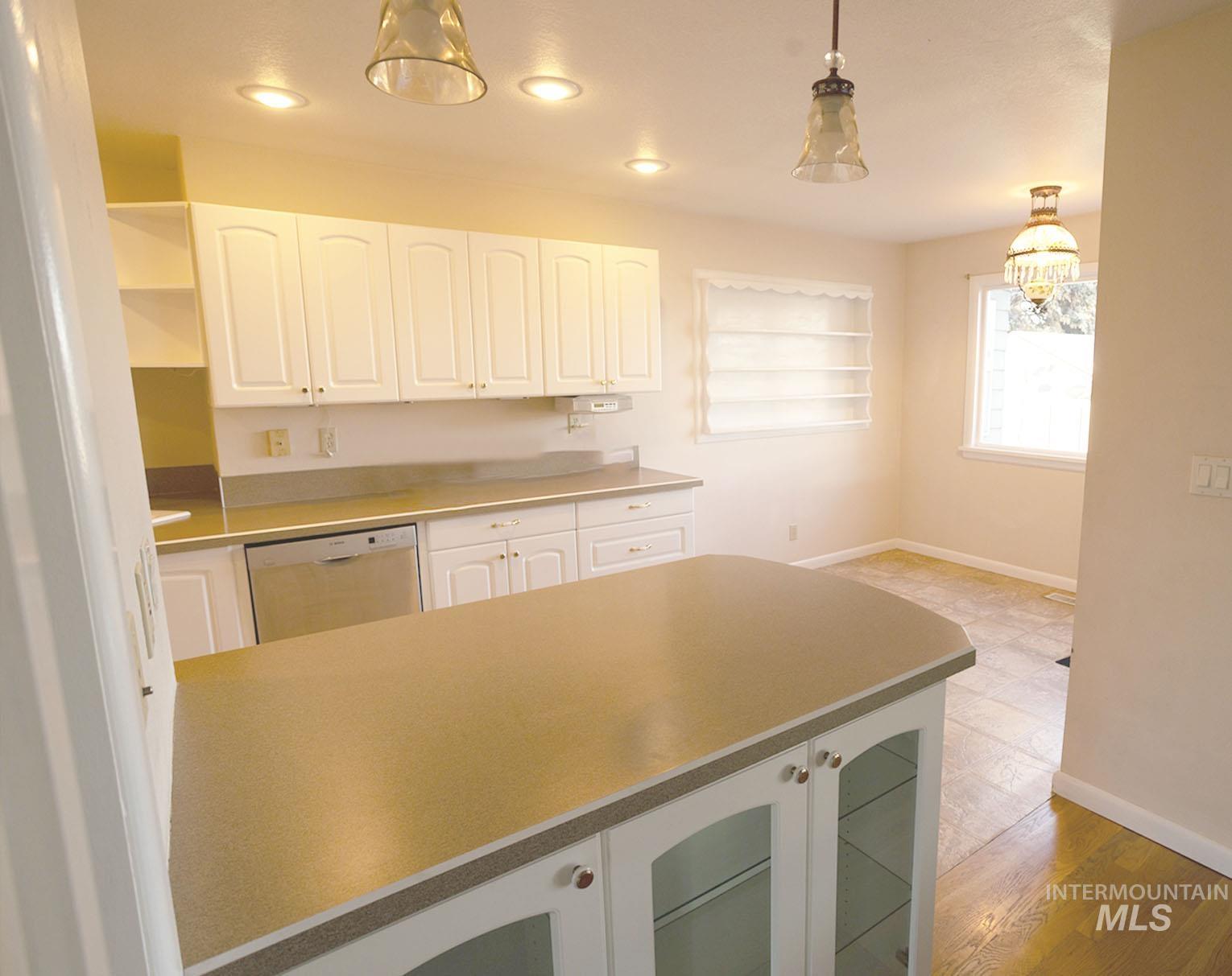 Kitchen featuring white cabinetry, stainless steel dishwasher, pendant lighting, recessed lighting, and light countertops