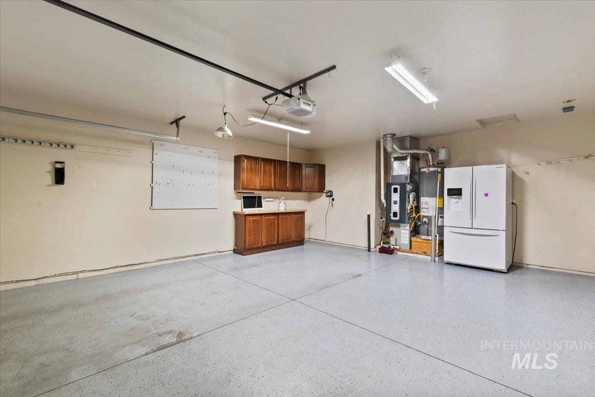 Garage featuring white refrigerator with ice dispenser, heating unit, gas water heater, and a garage door opener