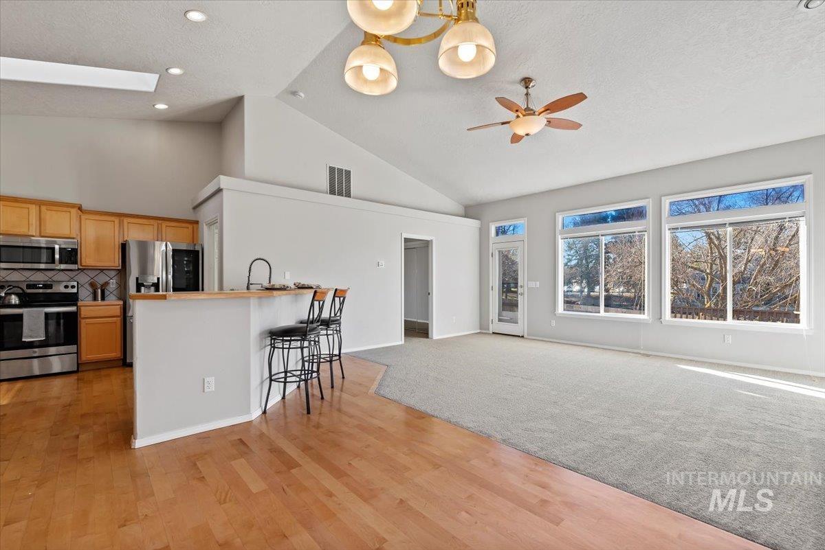 Kitchen featuring stainless steel appliances, decorative backsplash, a kitchen bar, open floor plan, and high vaulted ceiling