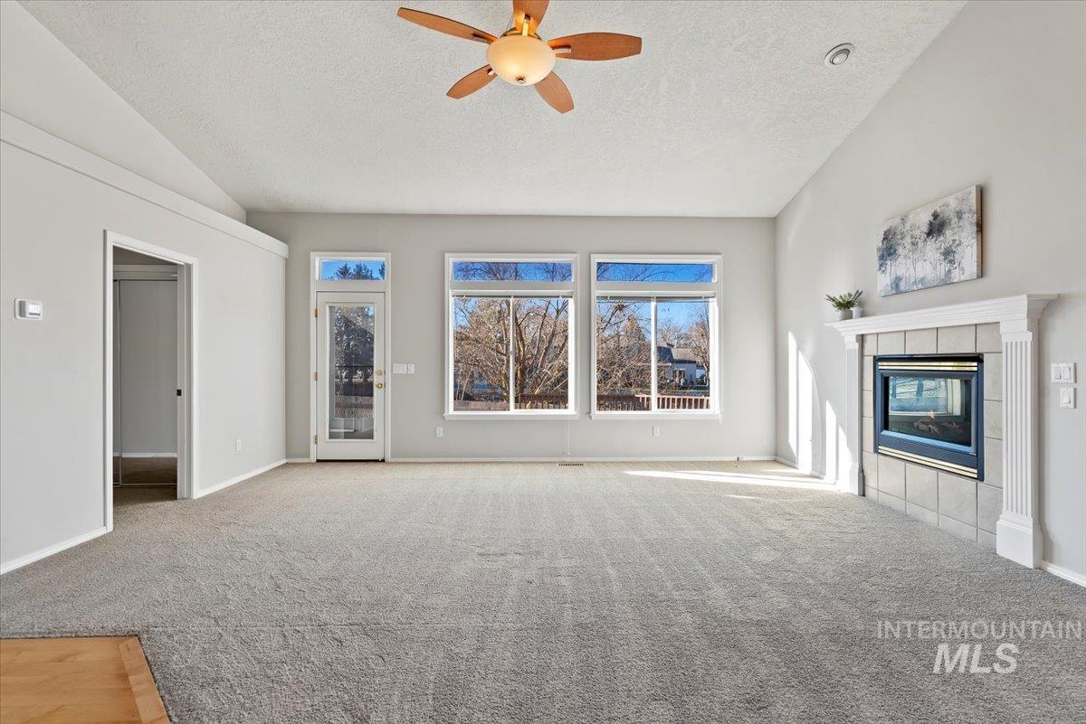Unfurnished living room with lofted ceiling, a textured ceiling, ceiling fan, light colored carpet, and a tile fireplace