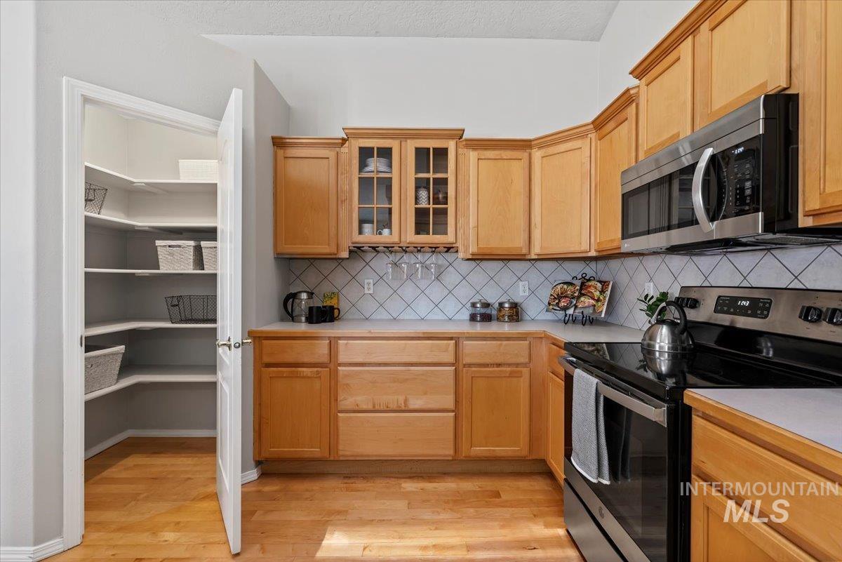 Kitchen featuring appliances with stainless steel finishes, light countertops, glass insert cabinets, light wood finished floors, and backsplash