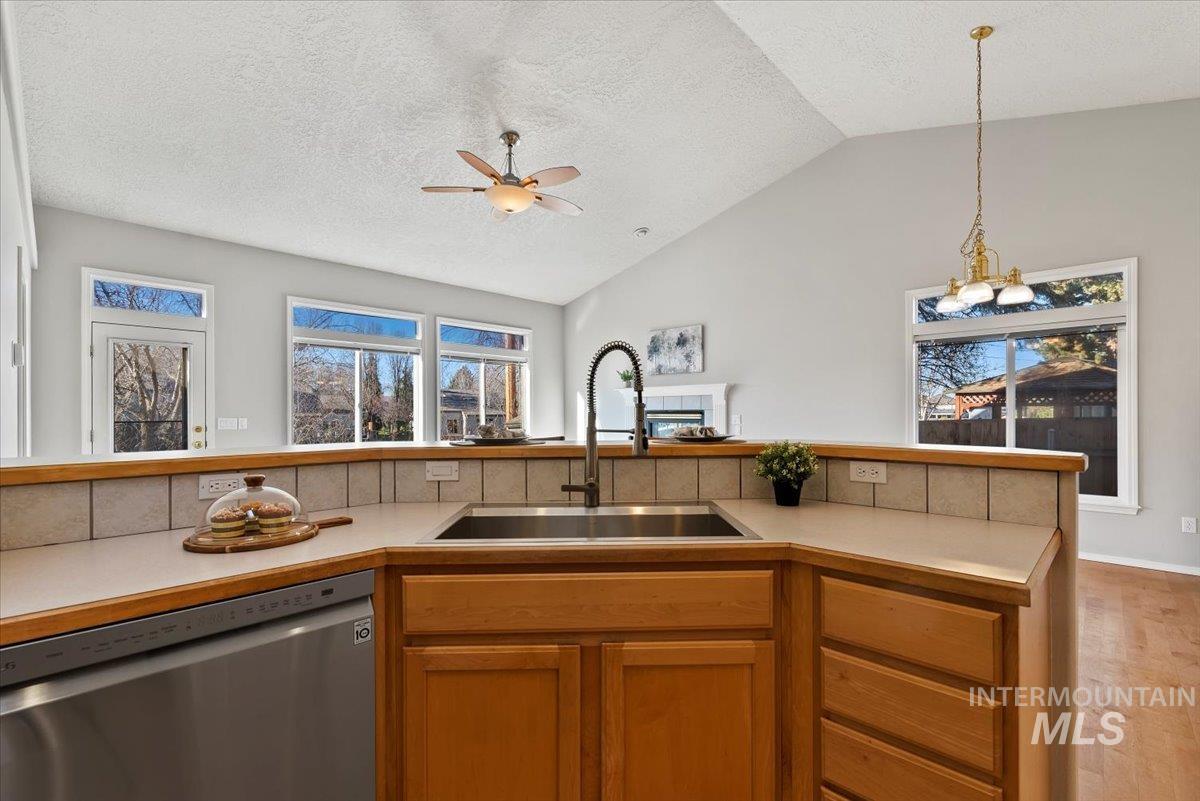 Kitchen featuring light countertops, dishwasher, hanging light fixtures, brown cabinets, and vaulted ceiling