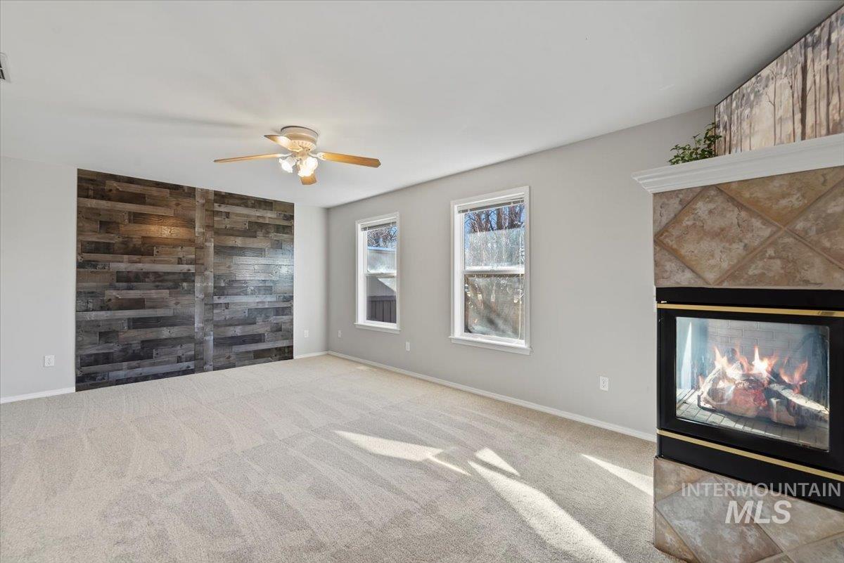 Unfurnished living room featuring a multi sided fireplace, carpet, wooden walls, an accent wall, and ceiling fan