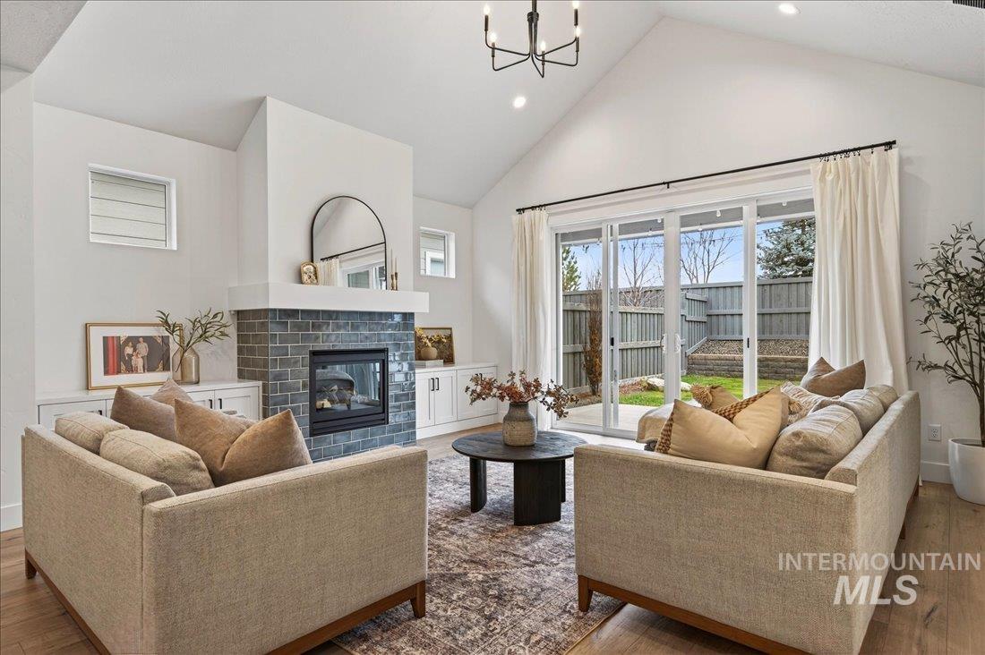 Living area with high vaulted ceiling, a glass covered fireplace, wood-type flooring, a chandelier, and recessed lighting