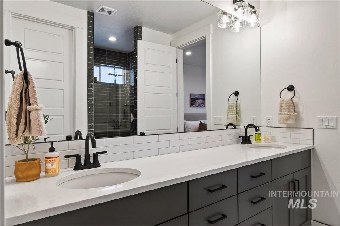 Bathroom featuring a shower stall, double vanity, ensuite bathroom, and backsplash