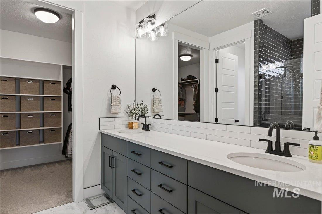 Full bathroom featuring a spacious closet, double vanity, a textured ceiling, light marble finish flooring, and a tile shower