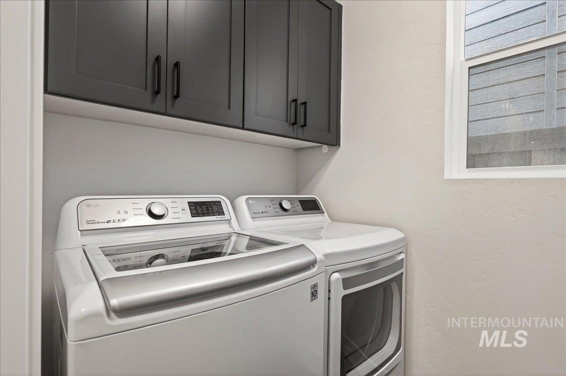 Washroom with a textured wall, separate washer and dryer, and cabinet space