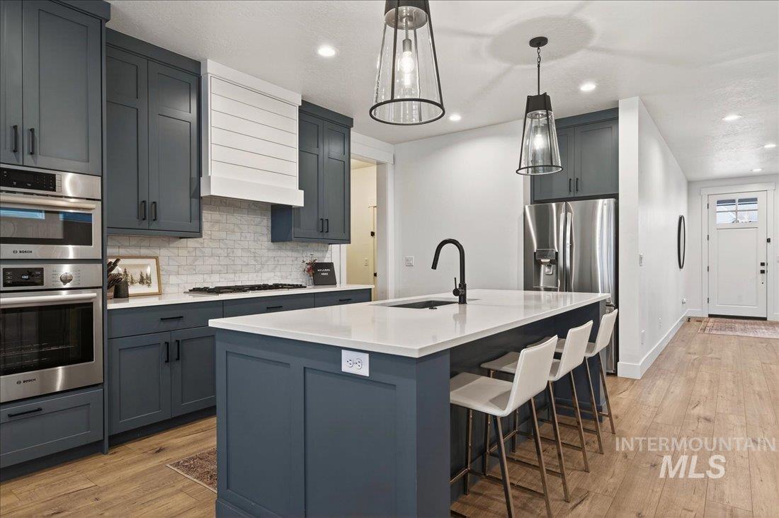Kitchen with a breakfast bar area, light wood-type flooring, gray cabinets, light stone countertops, and recessed lighting