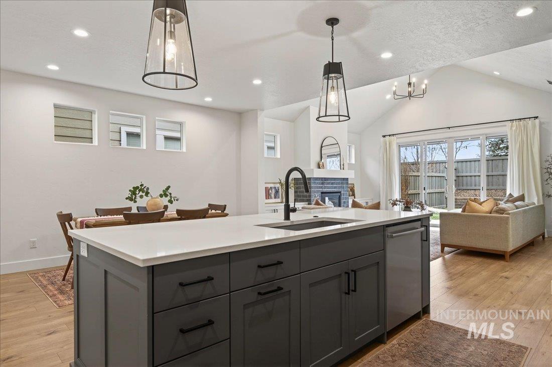 Kitchen with gray cabinets, light wood-style floors, open floor plan, pendant lighting, and an island with sink