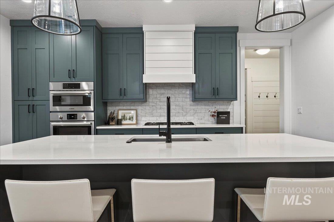 Kitchen featuring decorative light fixtures, a breakfast bar area, backsplash, light stone counters, and appliances with stainless steel finishes