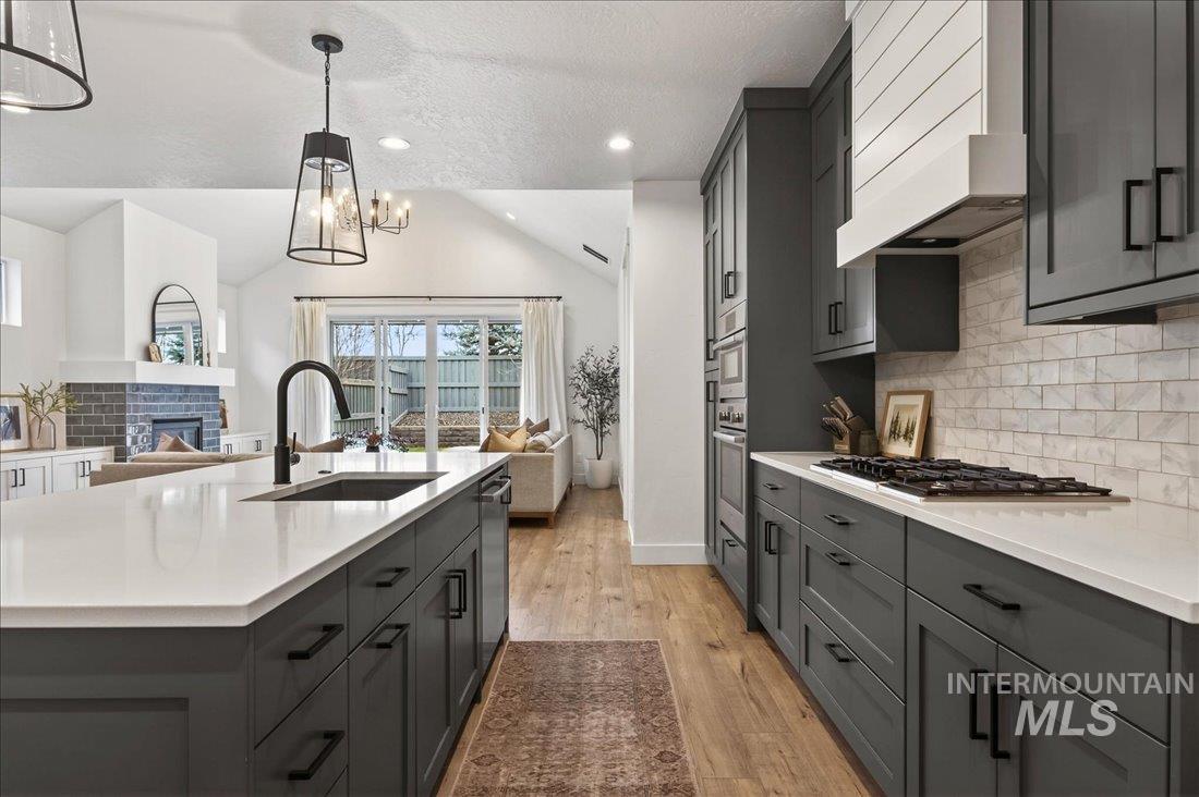 Kitchen featuring gray cabinetry, open floor plan, vaulted ceiling, light wood finished floors, and custom range hood