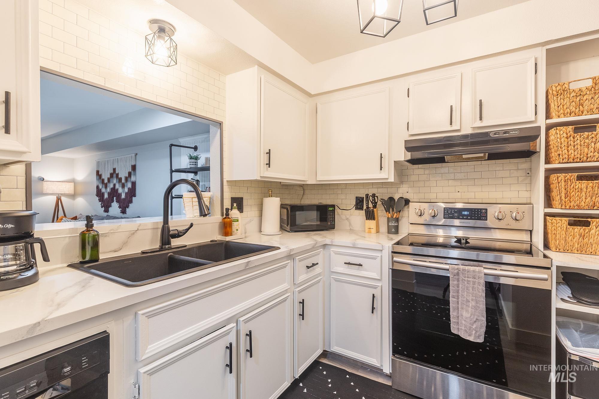 Kitchen with black appliances, under cabinet range hood, white cabinetry, decorative backsplash, and light stone counters