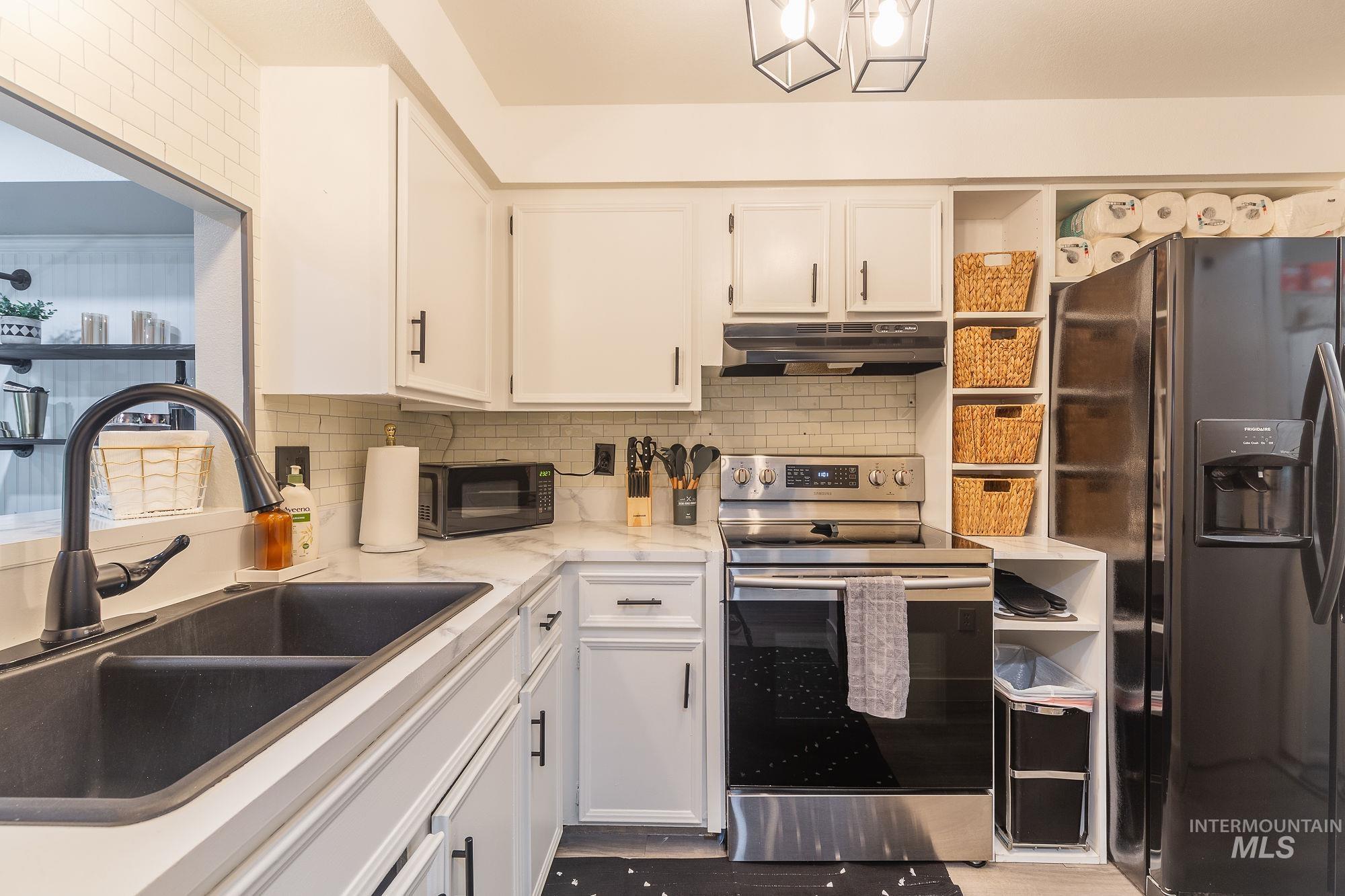 Kitchen with refrigerator with ice dispenser, under cabinet range hood, stainless steel electric range, black microwave, and white cabinets