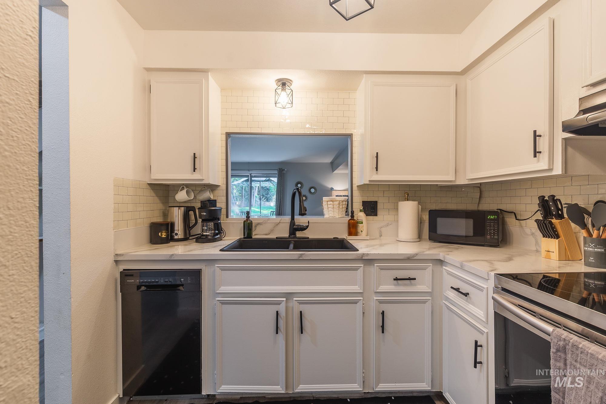 Kitchen featuring black appliances, tasteful backsplash, white cabinets, ventilation hood, and light stone countertops