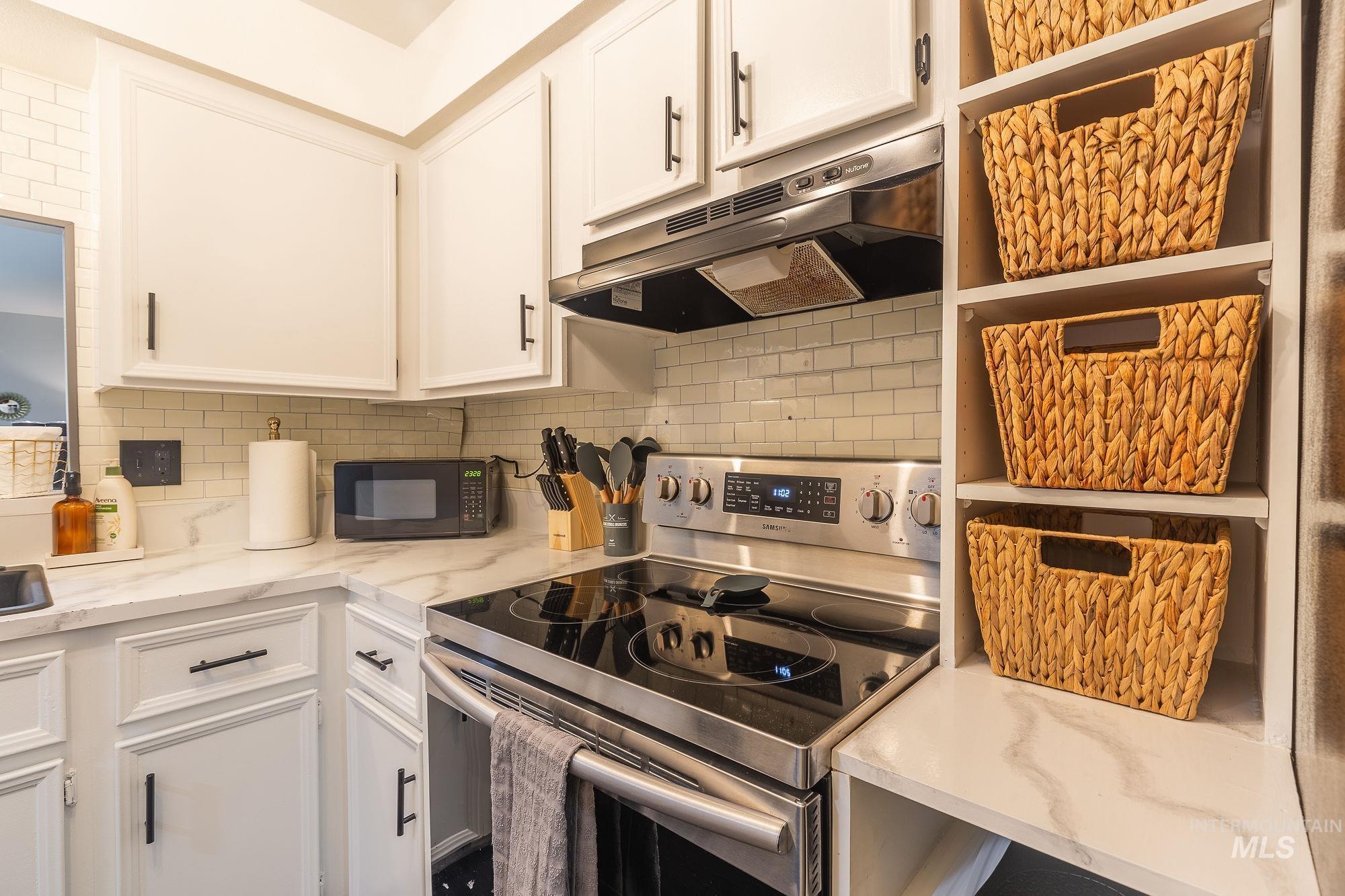Kitchen with stainless steel electric range, under cabinet range hood, black microwave, open shelves, and white cabinetry