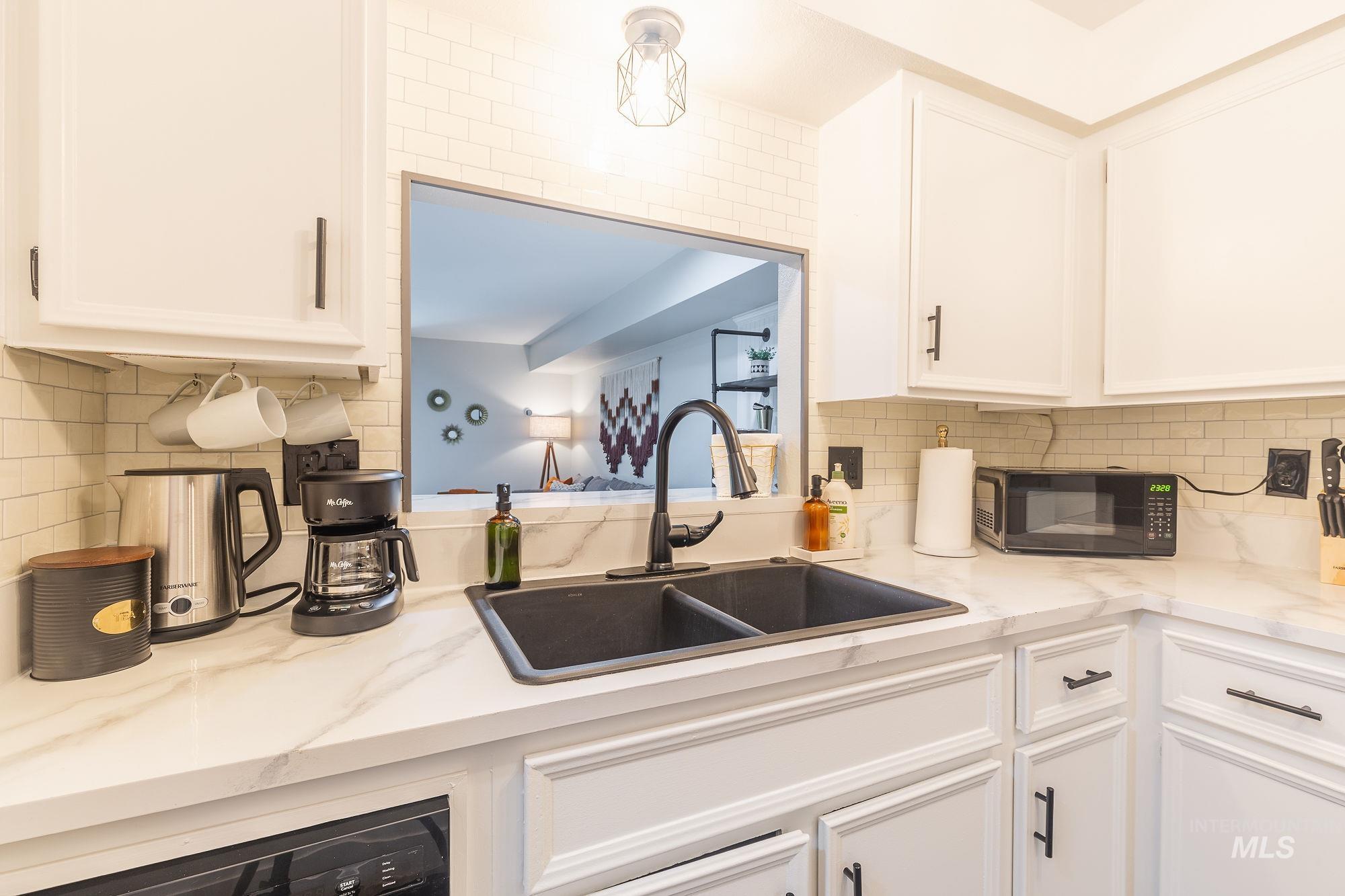 Kitchen featuring black microwave, white cabinetry, decorative backsplash, and light stone countertops