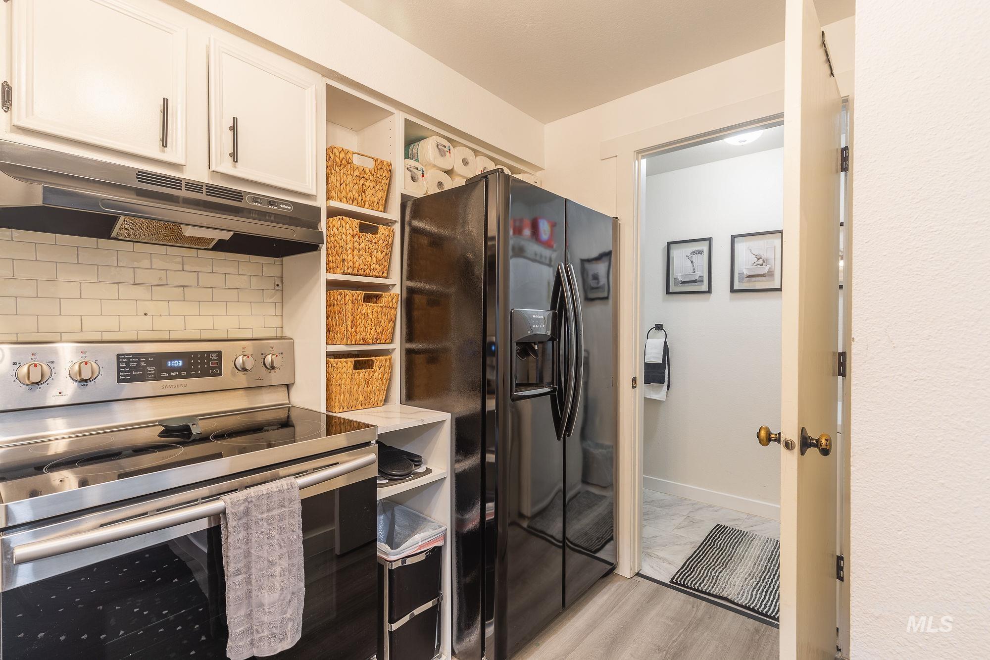 Kitchen with stainless steel electric range oven, black fridge, under cabinet range hood, tasteful backsplash, and white cabinets