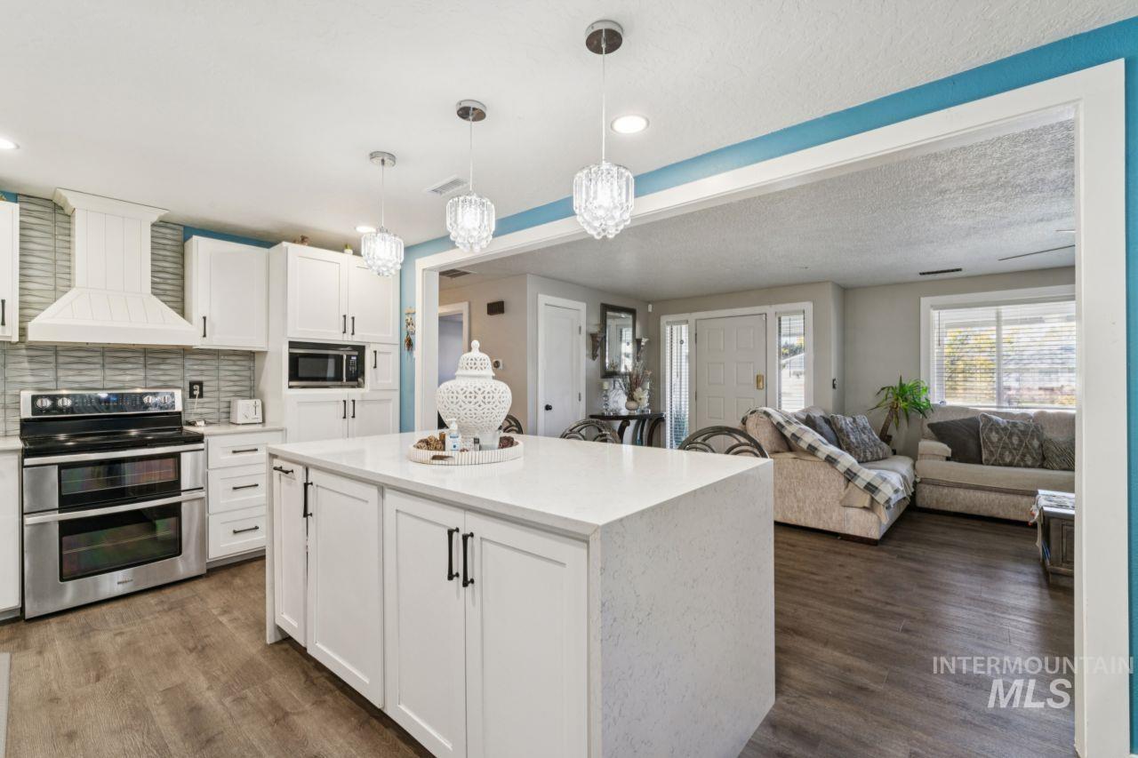 Kitchen featuring white cabinets, range with two ovens, custom range hood, decorative backsplash, and hanging light fixtures