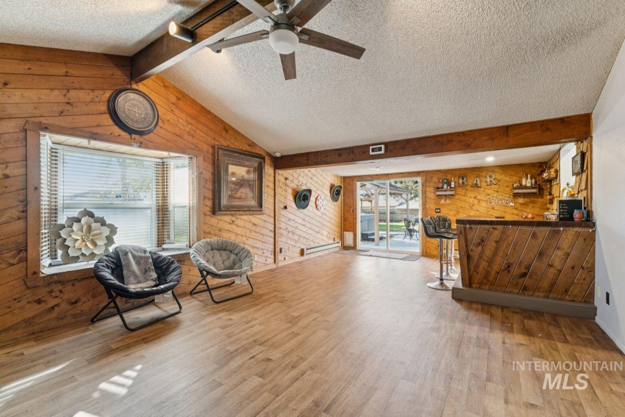 Living area featuring wood walls, a textured ceiling, light wood-style flooring, bar, and a baseboard radiator