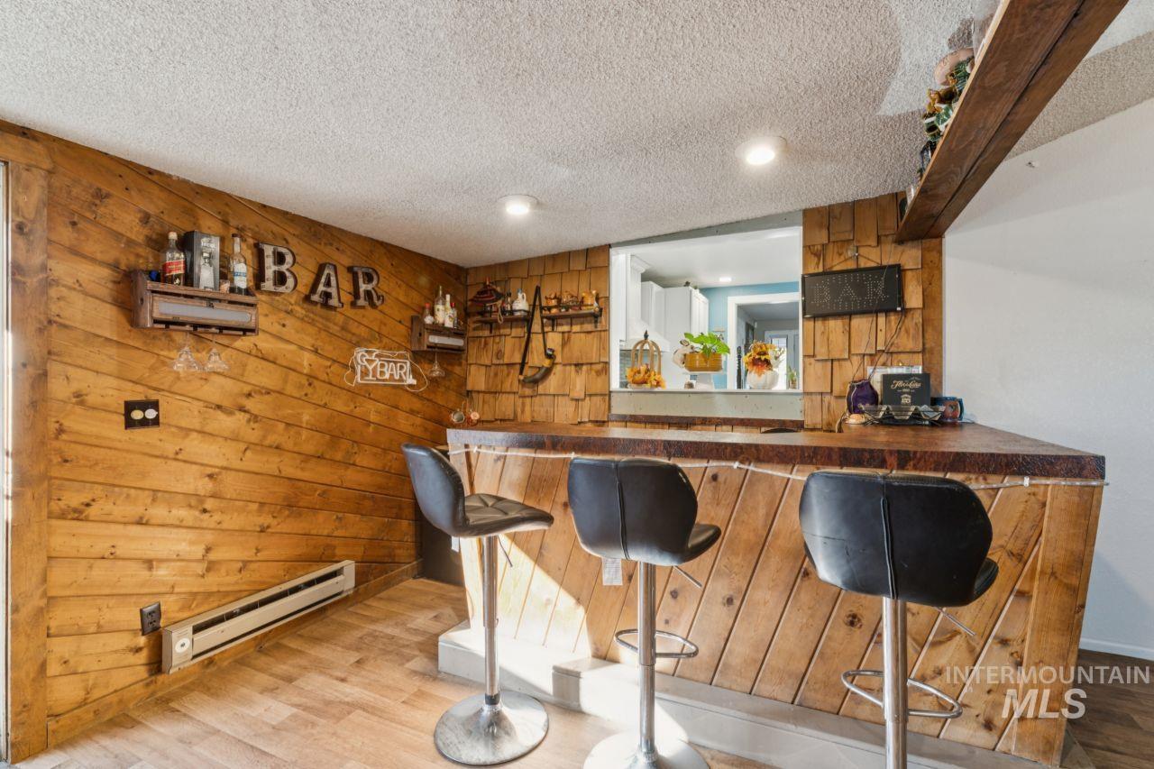 Indoor dry bar with wooden walls, wood finished floors, baseboard heating, and a textured ceiling