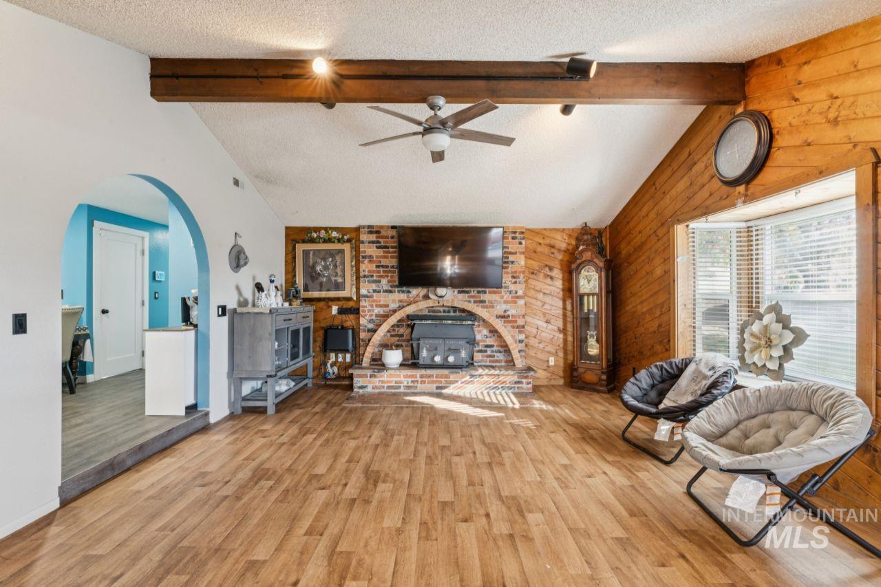 Living room with a textured ceiling, wood finished floors, wooden walls, arched walkways, and a ceiling fan