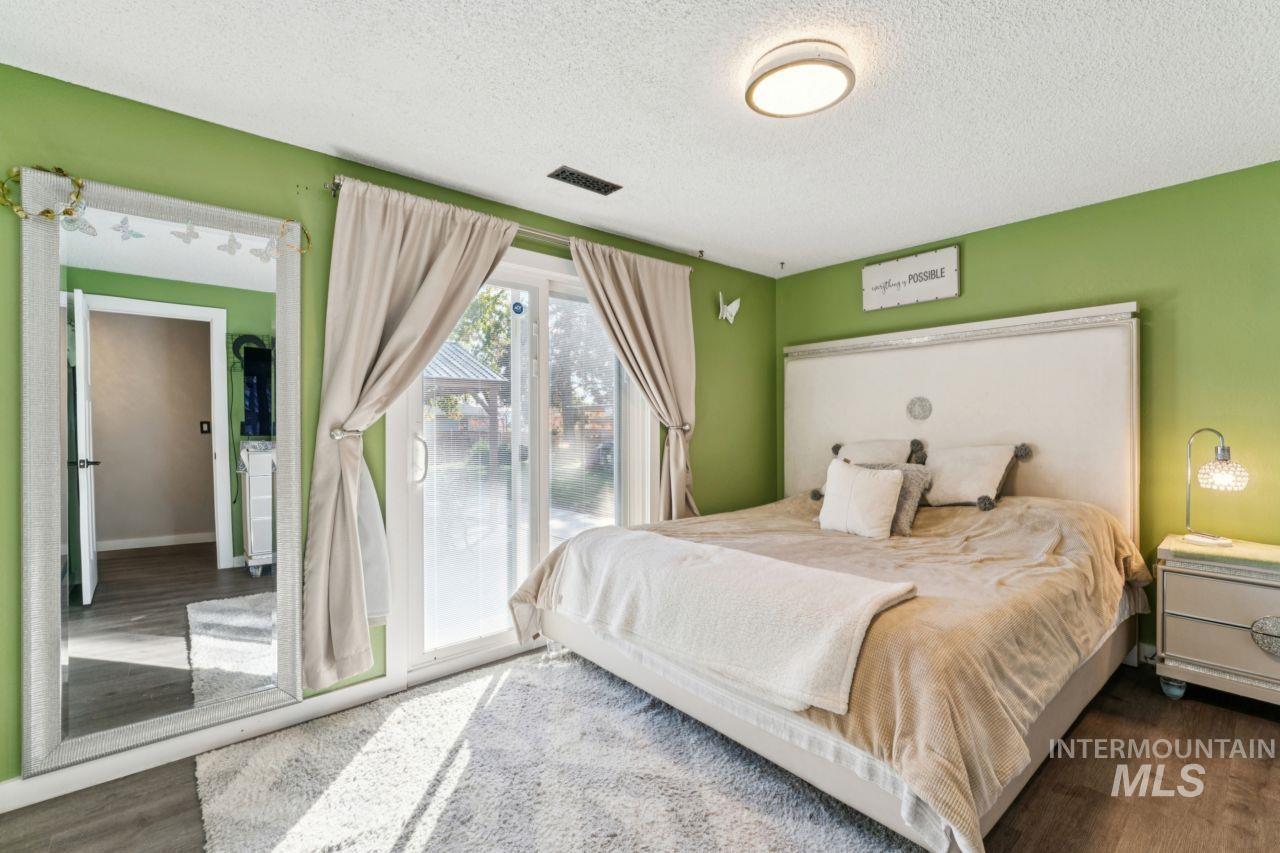 Bedroom with a textured ceiling, dark wood-style flooring, and access to exterior