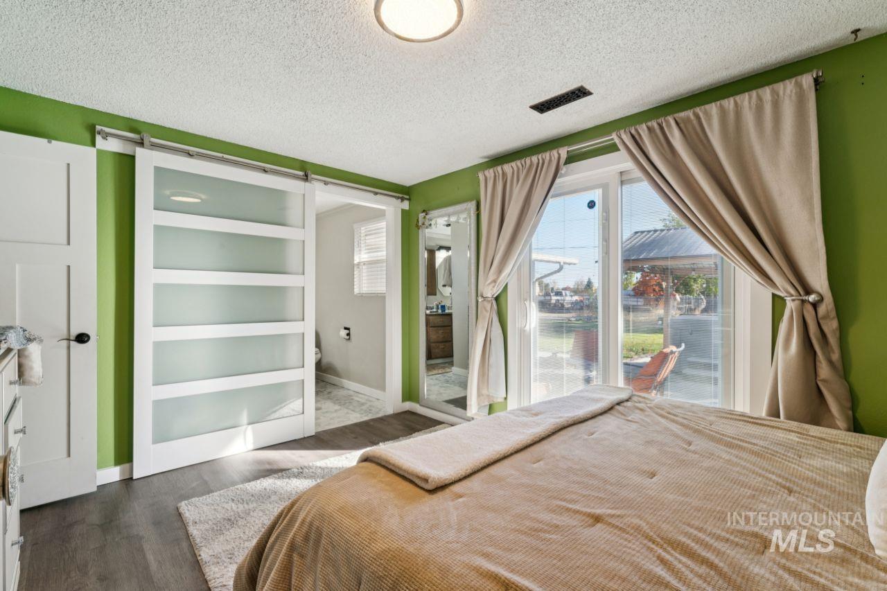 Bedroom with a barn door, a textured ceiling, dark wood-style flooring, access to outside, and connected bathroom