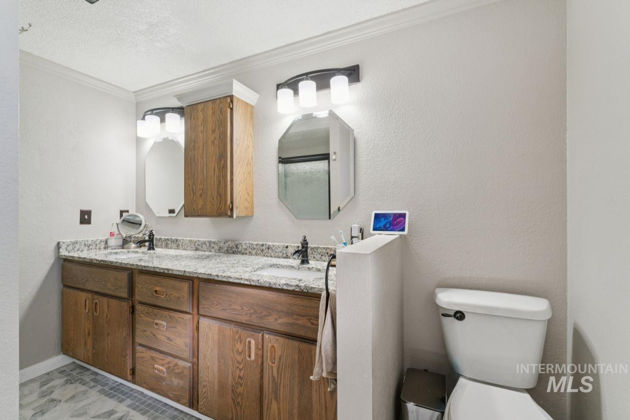 Bathroom with a textured wall, double vanity, ornamental molding, a shower with door, and a textured ceiling